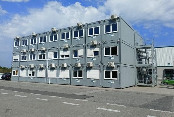 Viacpodlažná budova v šedej farbe z kancelárskych kontajnerov s oknami.